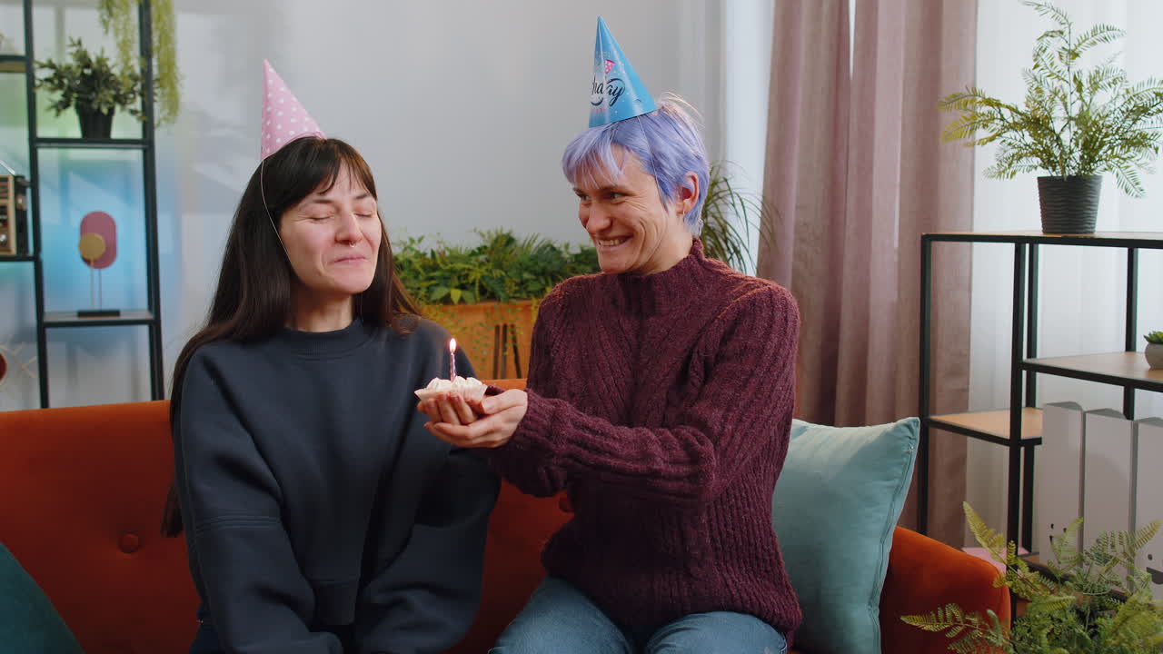 Lesbian women family celebrating birthday congratulating blowing burning candle on cake at home