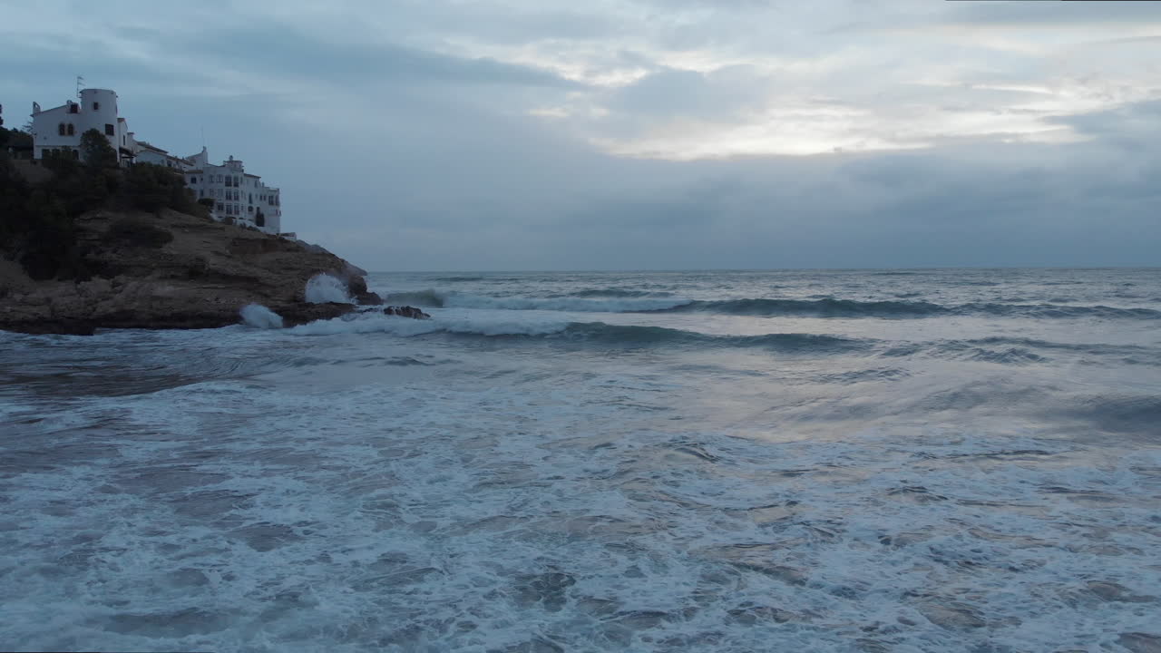 극적인 저공 비행 드론 샷, 이른 아침 시간 동안 바위가 많은 해안에서 들어오는 폭풍우가 치는 바다 파도 위로 활공
