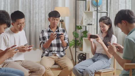 asian teen group sitting in chairs forming a circle playing game on smartphone at home