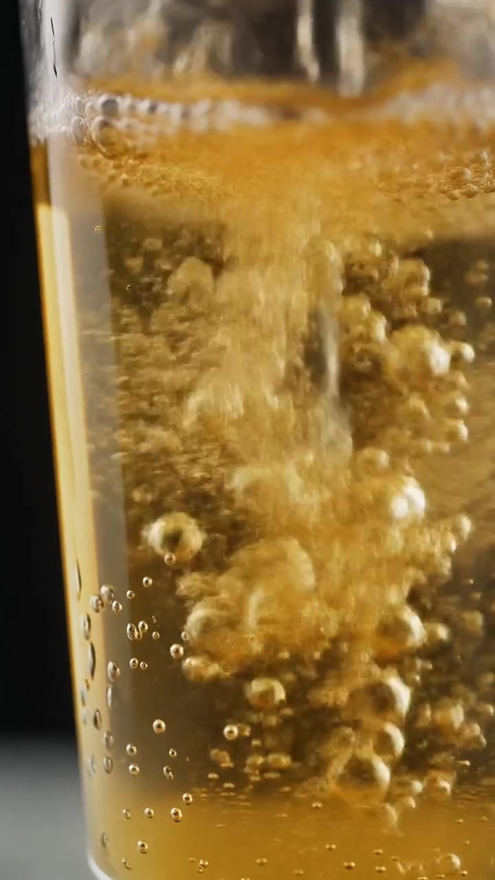 Refrigerante dourado gelado servido em um copo com gotas de condensação na superfície do vidro