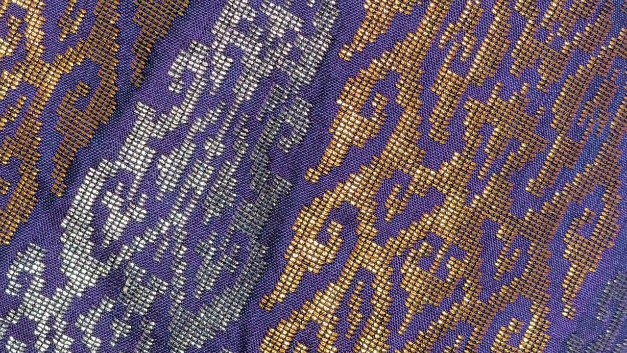 Detailed close-up of luxurious Songket fabric. The intricate gold embroidery shines across the handwoven surface. This prestigious Malaysian textile is reserved for the most special occasions.