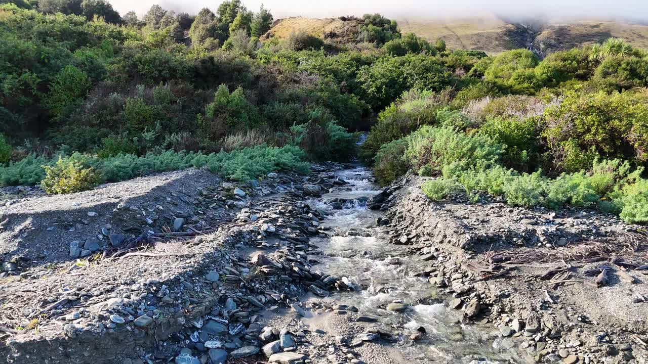 Aerial footage captures a serene glacial stream flowing through lush greenery in New Zealand, showcasing natural beauty and tranquility