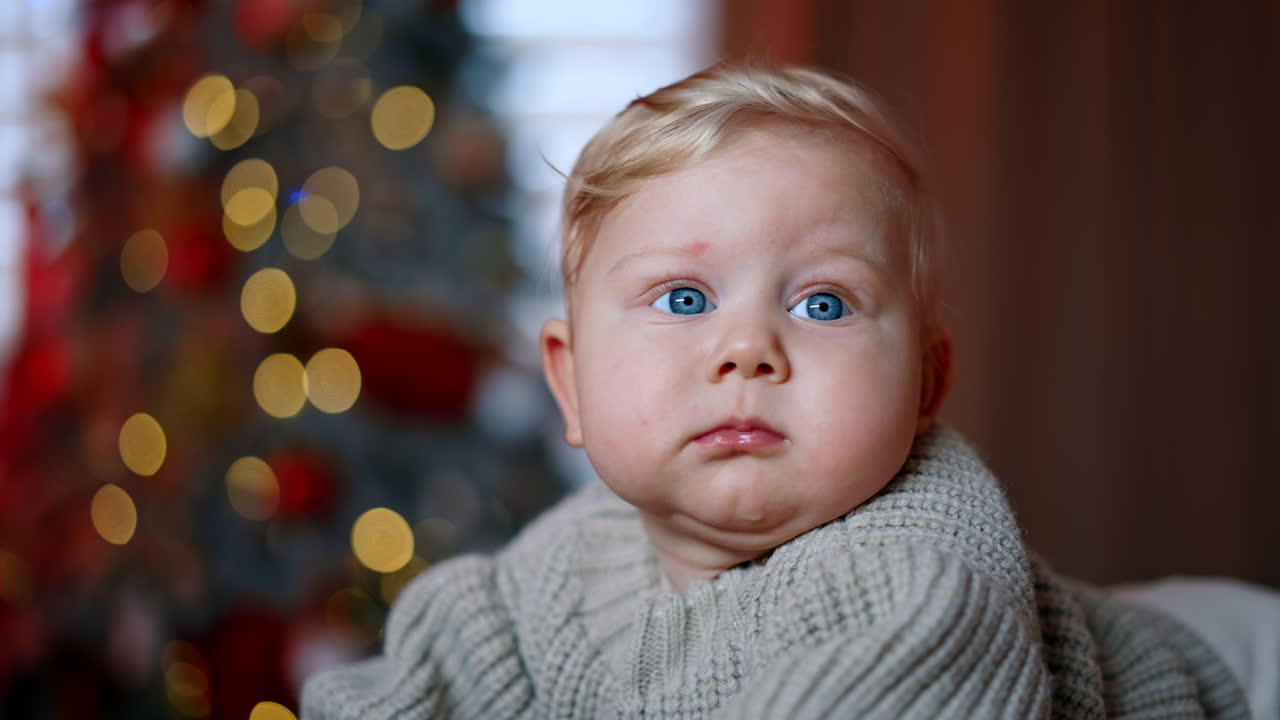 Adorable round-faced baby with big blue eyes lies on belly. Close up portrait of a child in grey sweater looking around.