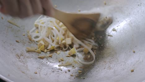 흰색 아시아 국수와 흰색 두부가 조리되고 팬에 빨간색 소스와 함께 볶으면서 팟타이를 만들 준비를 하고 있습니다.