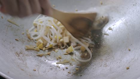 white asian noodle and white tofu while being cooked and stir fried with red source in the pan preparing to make pad-thai