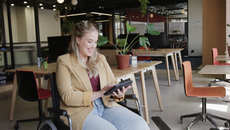 happy caucasian casual businesswoman in wheelchair using tablet in office, in slow motion