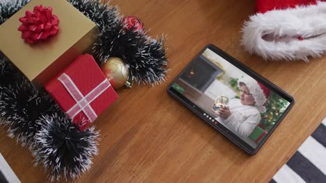 niño caucásico con sombrero de papá noel jugando con globo de nieve en la videollamada de navidad en la tableta
