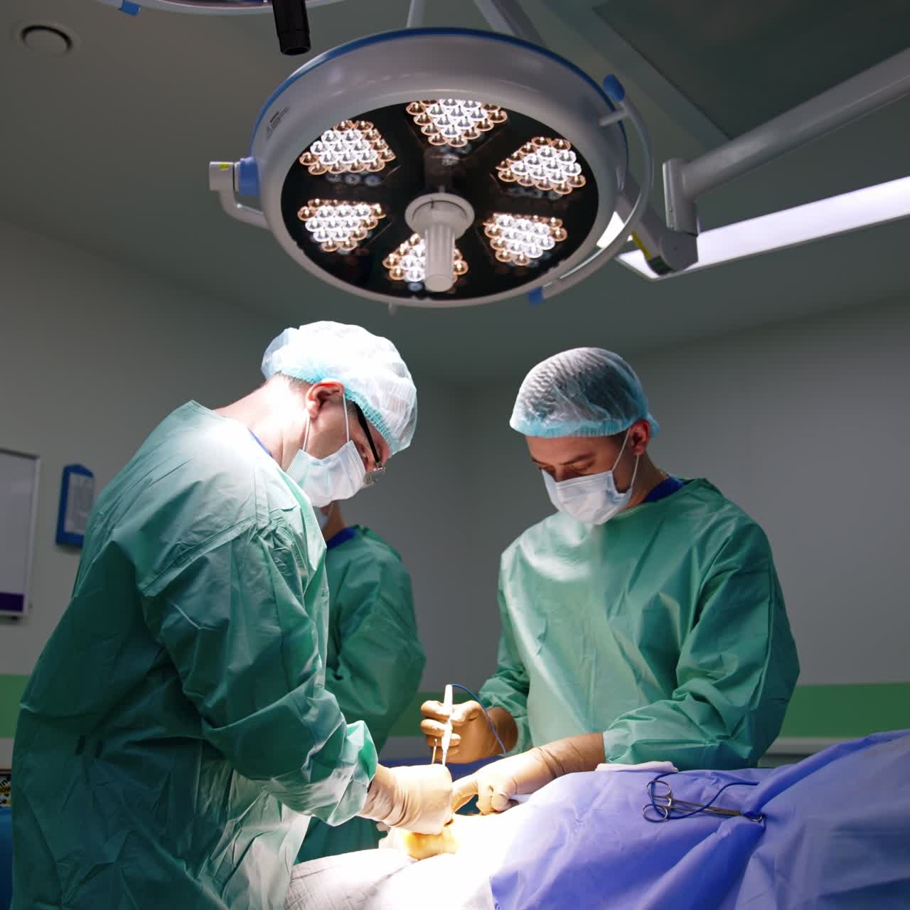 Ortopedici professionisti eseguono un'operazione. Chirurghi concentrati usano moderni strumenti metallici lavorando sotto potenti lampade.
