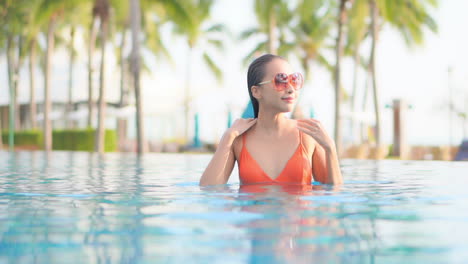 Sexy-asian-woman-on-tropical-vacation,-caresses-wet-hair-in-swimming-pool-on-hot-summer-day,-slow-motion