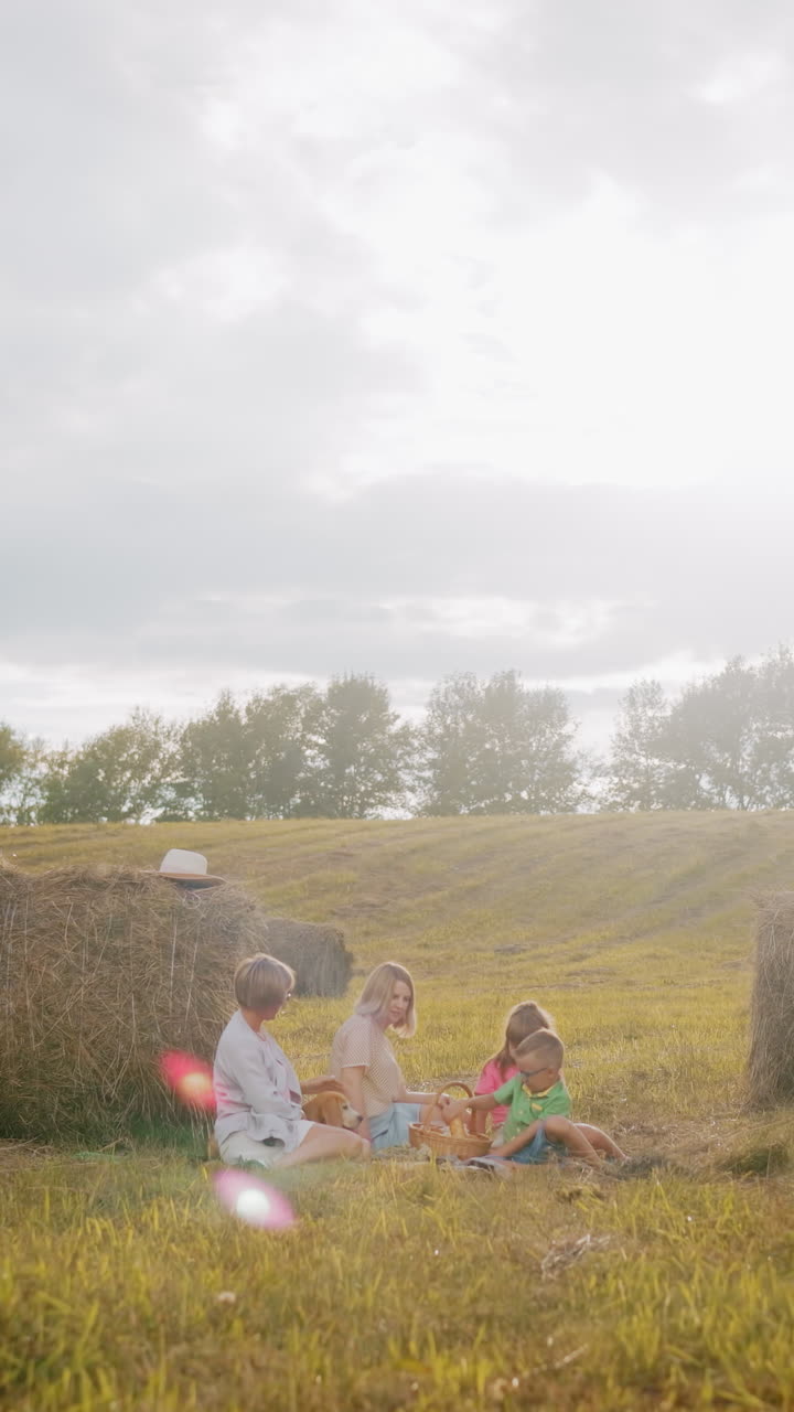 열린 시골에서 미니 피크닉을 즐기는 행복한 가족, 따뜻한 빛 빛과 카메라 플레어가 꿈 같은 분위기를 만드는 데기 사이에서 담요에 앉아