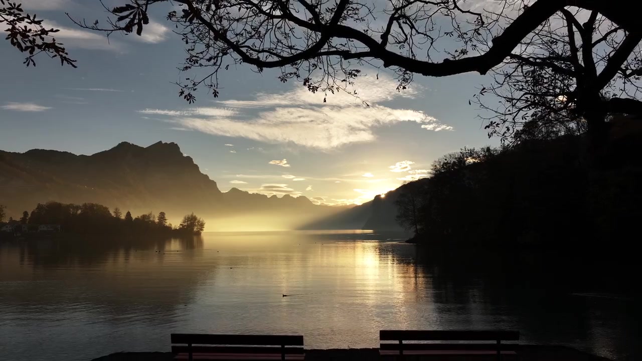 Sinar matahari pagi di atas Walensee dengan pegunungan berkabut dan pantulan di air yang tenang