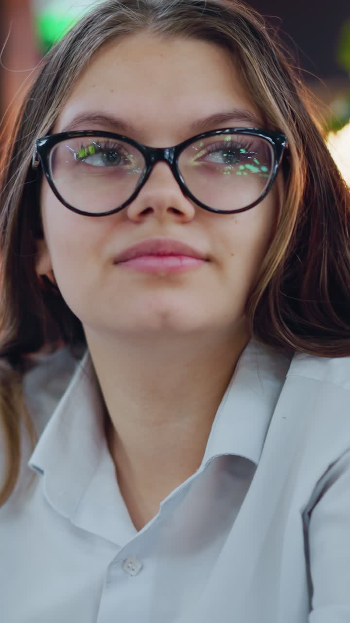 primer plano de una mujer elegante con gafas, teléfono operativo, girando a la izquierda con una mirada confiada, sentada en un bar elegante con iluminación cálida y vegetación exuberante, dedicada a la comunicación digital