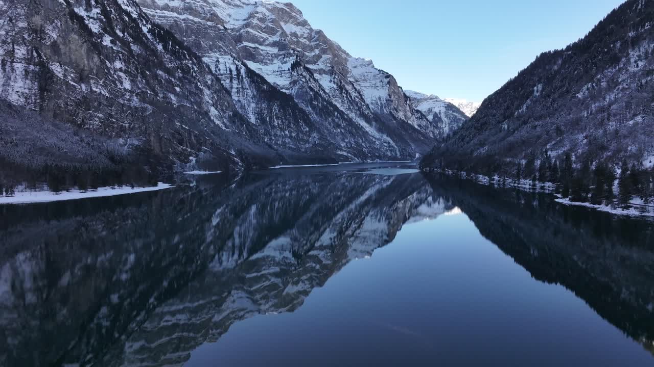 Aerial Klöntalersee reflecting snowy Alps in Klöntal, Switzerland, serene winter landscape