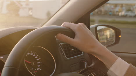 woman driver hands on steering wheel driving car in city on the road at rush hour travelling to destination at sunset