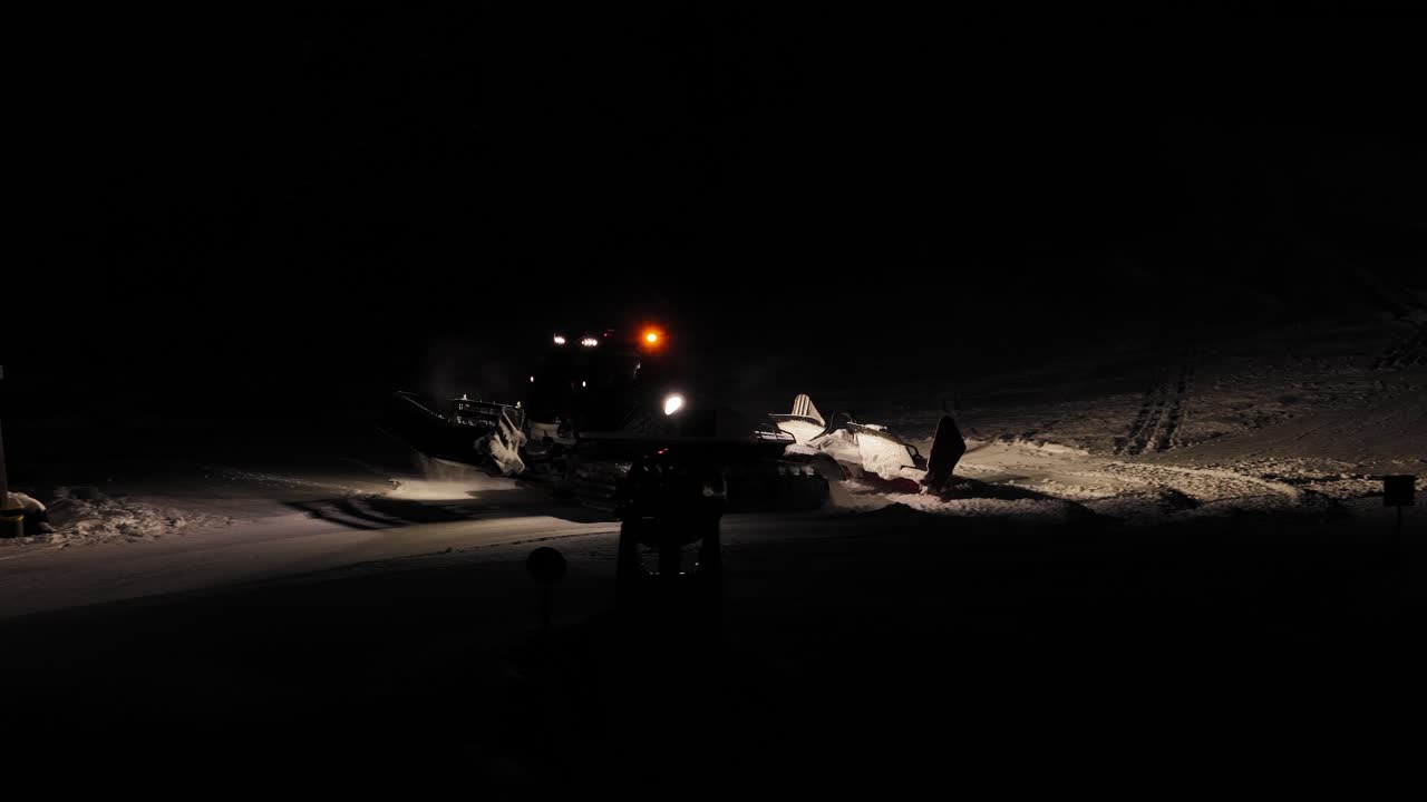 Heavy industrial machinery, nighttime environment, ski slope preparation