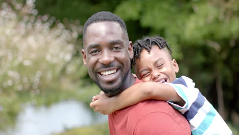 padre afroamericano con barba abraza a un hijo afroamericano alegre en casa