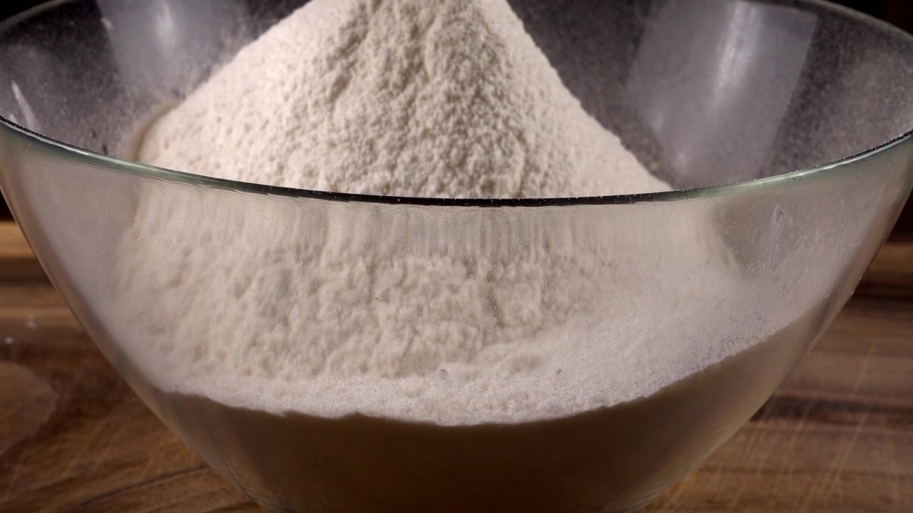 Mengayak tepung menggunakan saringan ke dalam mangkuk kaca di dapur.
