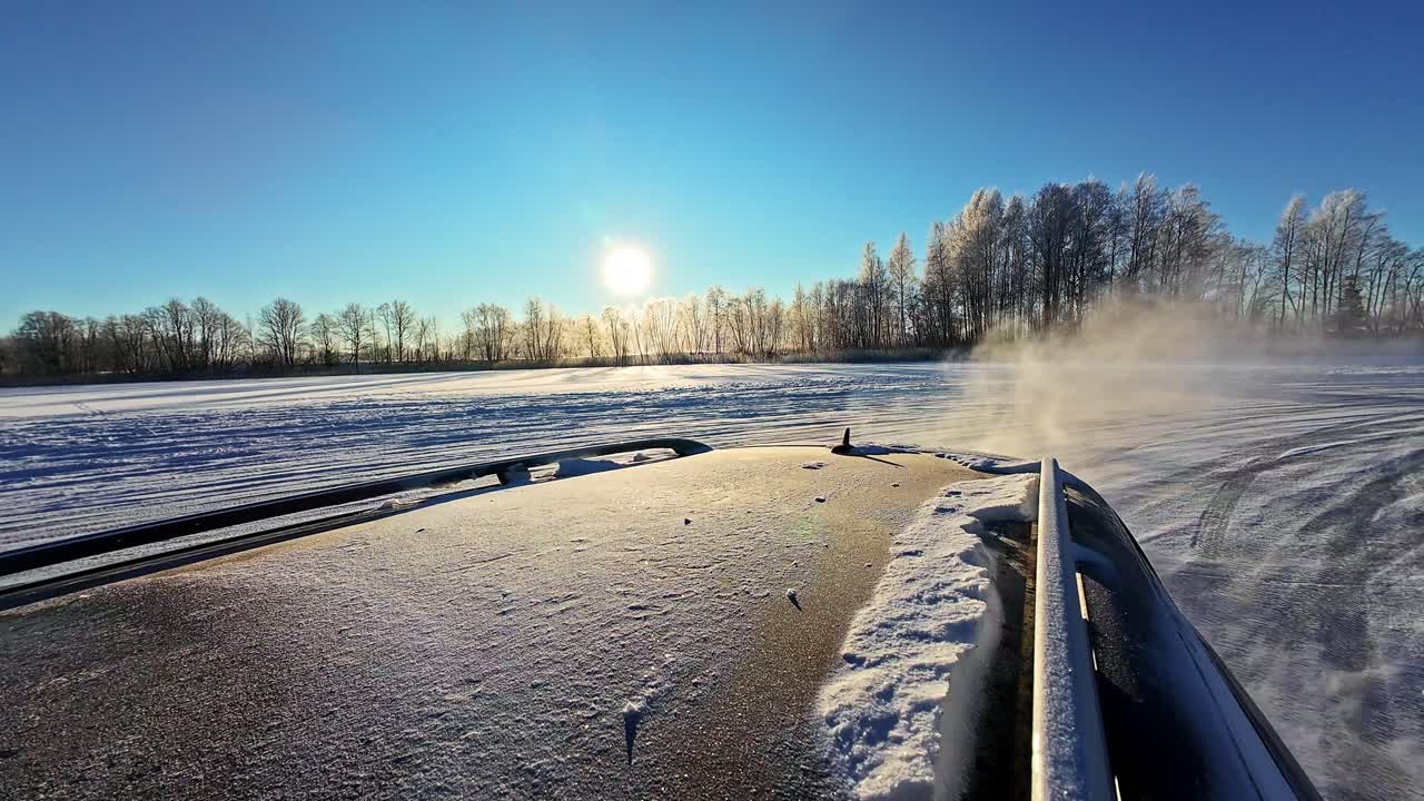 Blick vom Autodach: Driften durch verschneite Landschaft, tiefstehende Sonne hinter Bäumen in Zeitlupe.