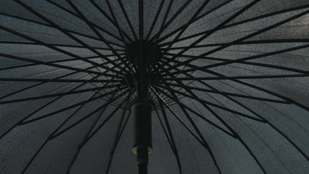 under umbrella canopy at night radial spokes glisten with raindrops, dim streetlight casts soft glow, wet fabric texture emphasized, closeup underside perspective evokes solitude and shelter