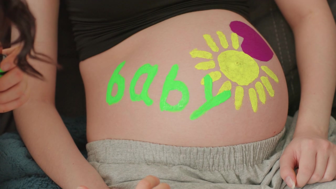 Pittura a mano con design 'Baby' e sole sulla pancia di una donna incinta
