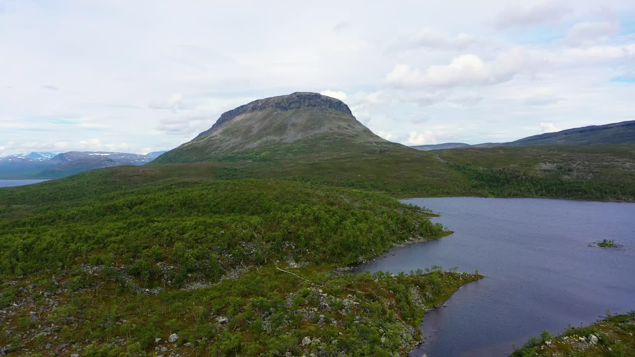 Aerial, rising, drone shot over lake Tshahkajarvi, towards the Saanatunturi fell, on a cloudy, summer day, in Kilpisjarvi, Enontekio, Lapland, Finland