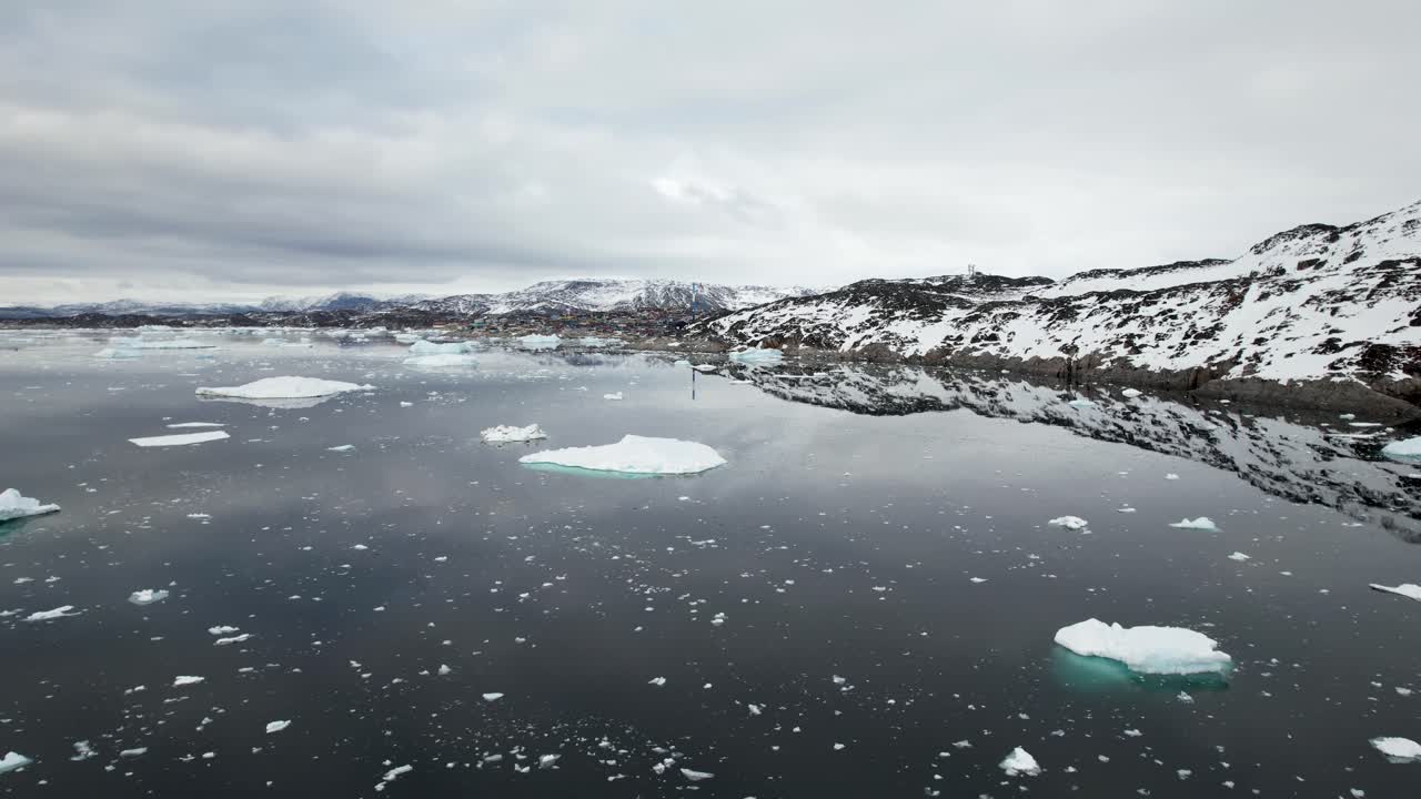 Incredibile paesaggio della Groenlandia ripreso da drone, con sorvolo di iceberg e riflessi sull'acqua, cielo drammatico