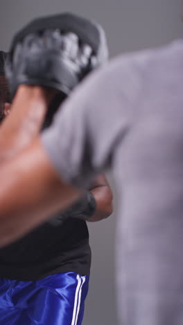 Vertical-Video-Studio-Shot-Of-Male-Boxer-Sparring-Working-Out-With-Trainer-Wearing-Punch-Mitts-Or-Gloves-Practising-For-Fight-2