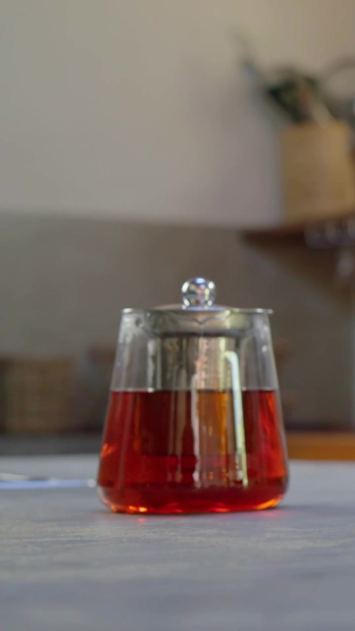 Video verticale: Mani con unghie rosse che tengono il telefono sul tavolo, sollevando una tazza sul piattino, mostrando una teiera.