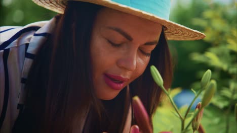 woman in straw hat gently smelling vibrant flowers in a lush garden, enjoying nature's beauty