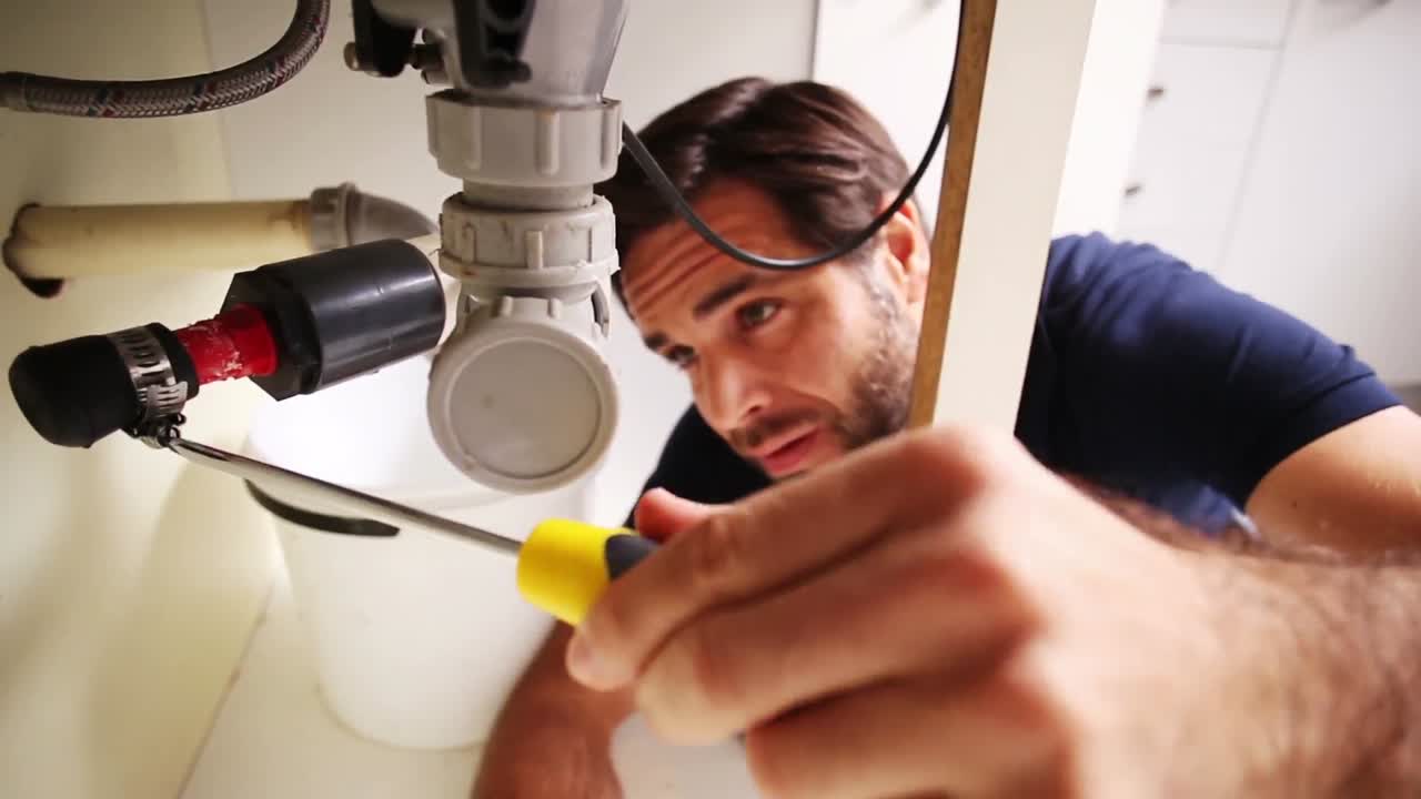 apuesto fontanero usando un destornillador para arreglar el fregadero