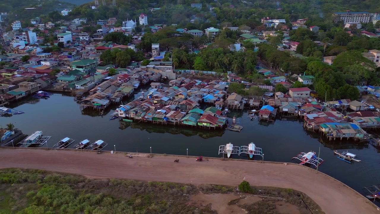 Dense case galleggianti su palafitte costruite sull'acqua accanto a un molo, che rappresentano la comunità e la vita tradizionale. Incredibile ampia panoramica aerea con drone.