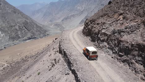 Discovering-Pakistan,-Aerial-View-of-Off-road-Vehicle-on-Hillside-Dirt-Road-Above-Canyon,-Tracking-Drone-Shot