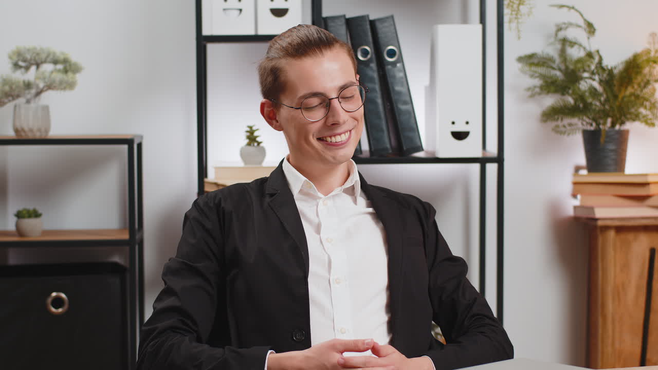 Smiling young businessman closing laptop after finishing work and taking break at home office table