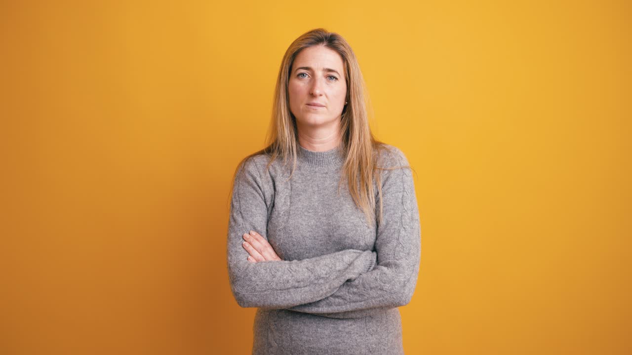 Serious Woman Standing with Arms Crossed on Yellow Background