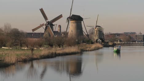 a boat moves along a canal in holland with windmills nearby 1