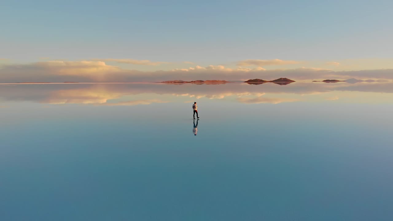 Aerial of a lone figure walking along the mirrored reflection of the world's largest salt flat in Uyuni Salt Flats , Bolivia