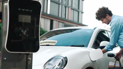 progressive businessman unplugs charger plug from charging point to his ev car.