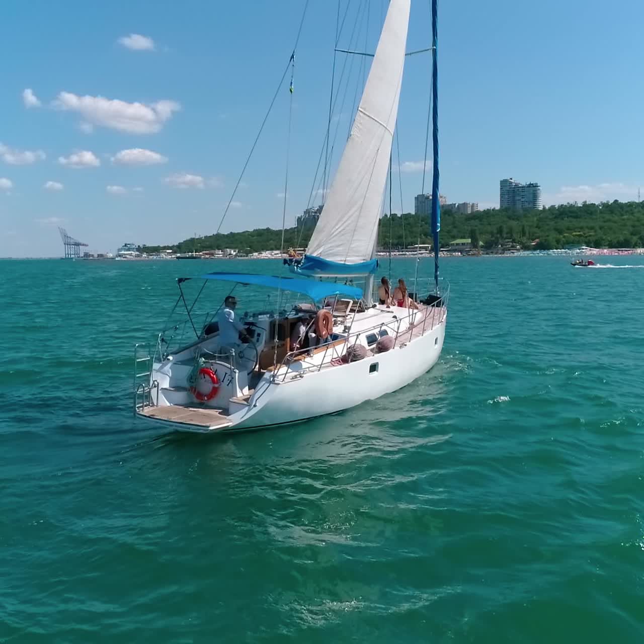 White yacht with sails floating to the shore. Beautiful sailboat with a few people on the sea in bright sunny day. Aerial view