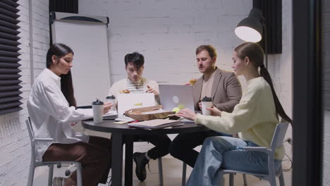 groep multi-etnische collega's die pizza eten en afhaalkoffie drinken tijdens een teamvergadering in de directiekamer