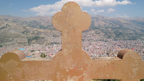 an aerial shot rises and tilts down, revealing the sprawling huaraz cityscape behind the large stone cross at the famous rataquenua viewpoint in the peruvian andes
