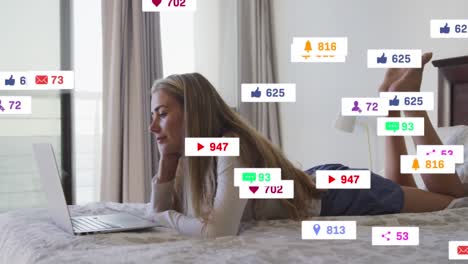 animation of network social media icons over smiling relaxing on bed using laptop