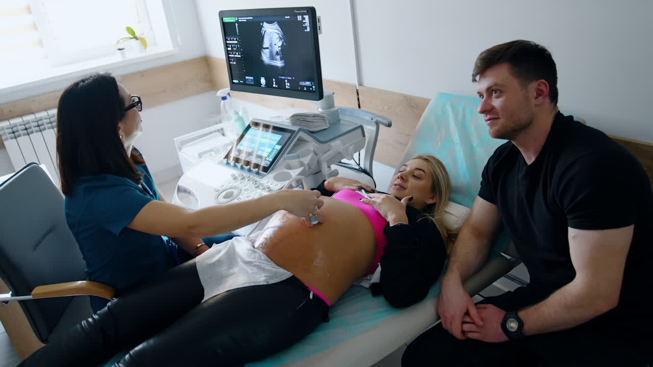 Future parents are visiting a doctor and having ultrasound pregnancy check up. Expecting parents see the baby on the monitor. Top view.