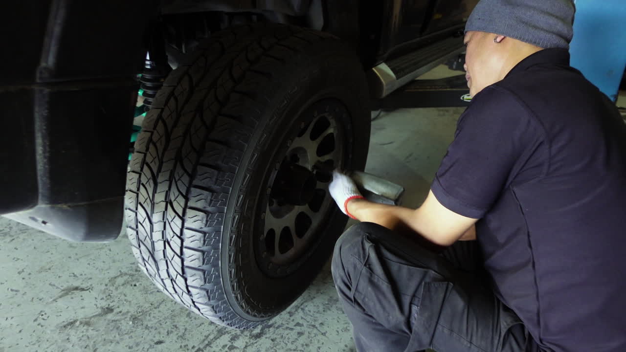 disparo en cámara lenta de un mecánico fijando una rueda en un suv usando una pistola de aire de impacto