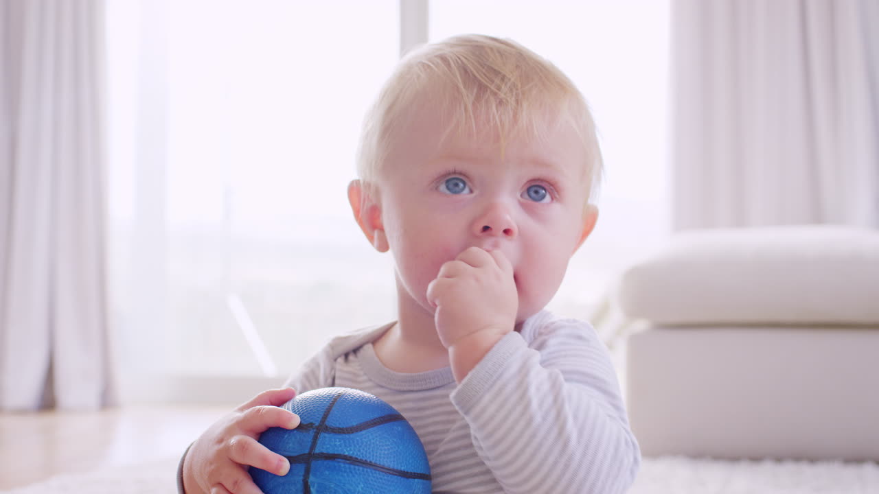 niño pequeño blanco sosteniendo y masticando una pelota, de cerca