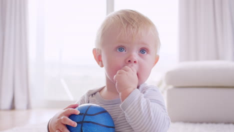 White-toddler-boy-holding-and-chewing-ball,-close-up
