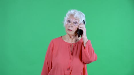 retrato de una mujer mayor mirando a la cámara y hablando en su teléfono inteligente. abuela de cabello gris en blusa roja en pantalla verde en el estudio. cerca