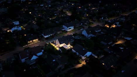 cyclist with light riding on street of american neighborhood at night. aerial flyover shot. lighting buildings and homes in american town. wide shot. quiet and peaceful residential area.