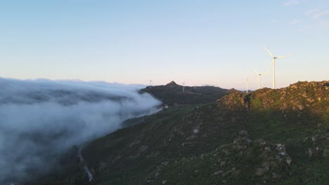 Wind-turbines-spinning-on-mountain-at-sunrise-and-clouds-on-valley,-Caramulo-in-Portugal