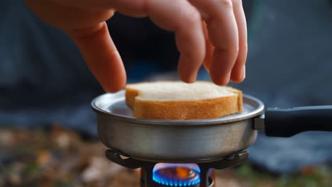 hand toasting bread on a portable camping stove