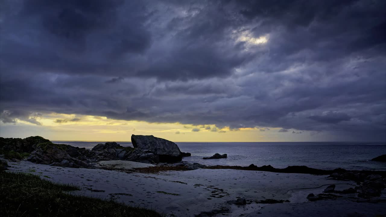 Dramatic Arctic coastal landscape with Dramatic clouds. Time Lapse. Rocky shore, sandy beach covered with seaweed in bright summer night. Lofoten Islands, Northern Norway.